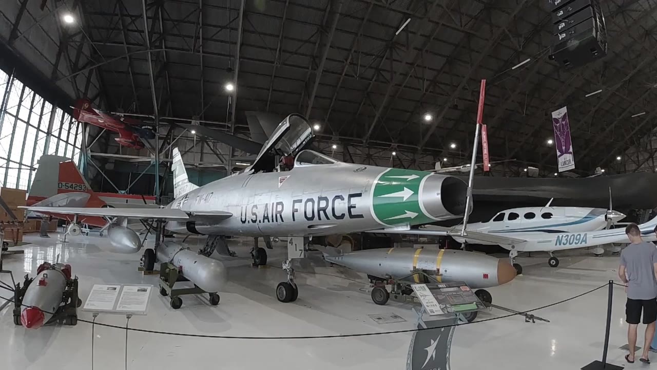 Wide interior view of an aircraft museum hangar in Denver, Colorado, showing a silver U.S. Air Force jet with a green nose cone on display under an arched roof with large windows; no visible people
