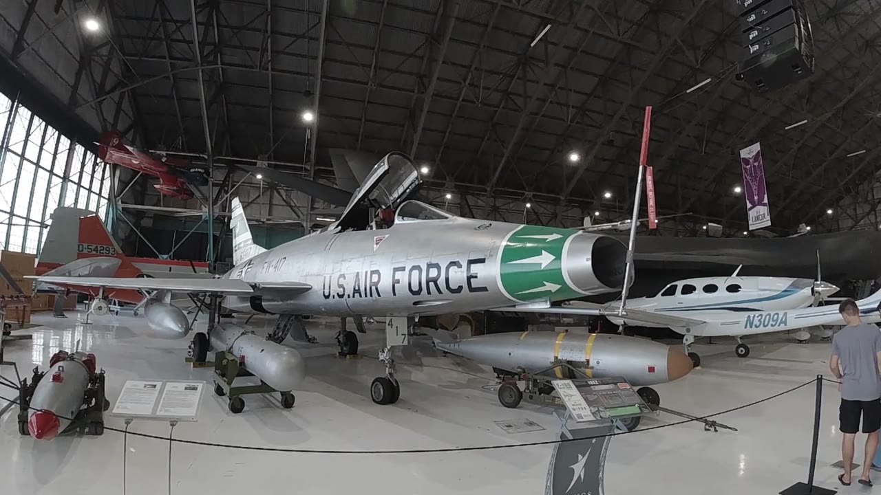 Wide museum hangar interior with silver U.S. Air Force jet centered under arched roof and overhead lighting
