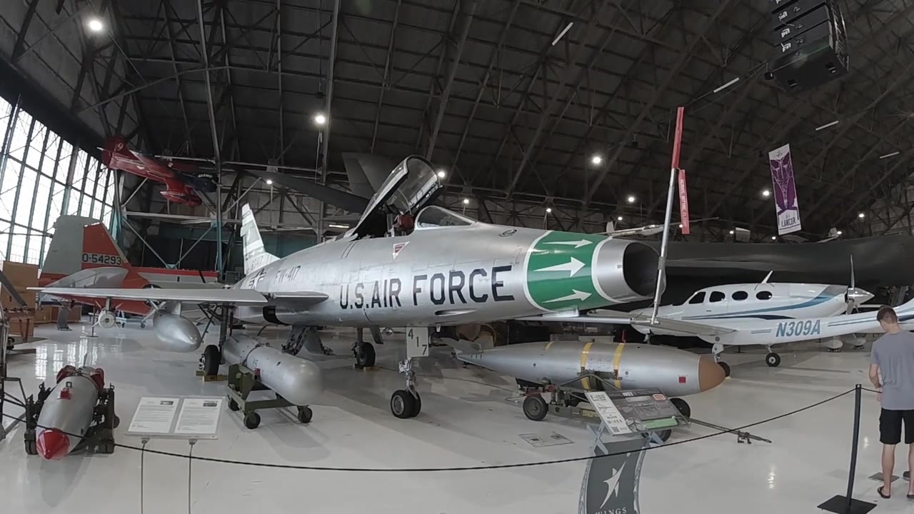 Wide aviation museum hangar interior in Denver showing a silver military jet with green nose cone; large windows line the left wall and no people are visible