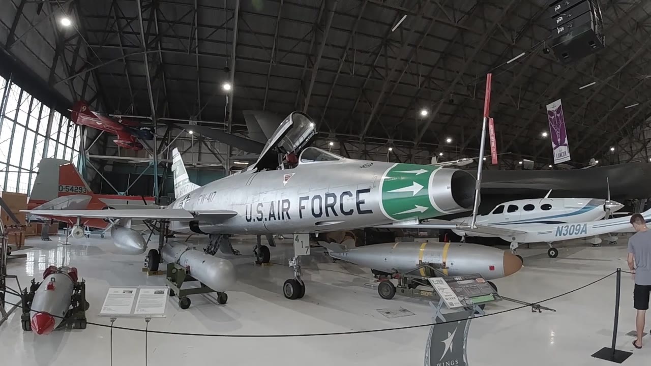 Museum hangar interior with silver Air Force jet on display, green nose cone, and background aircraft