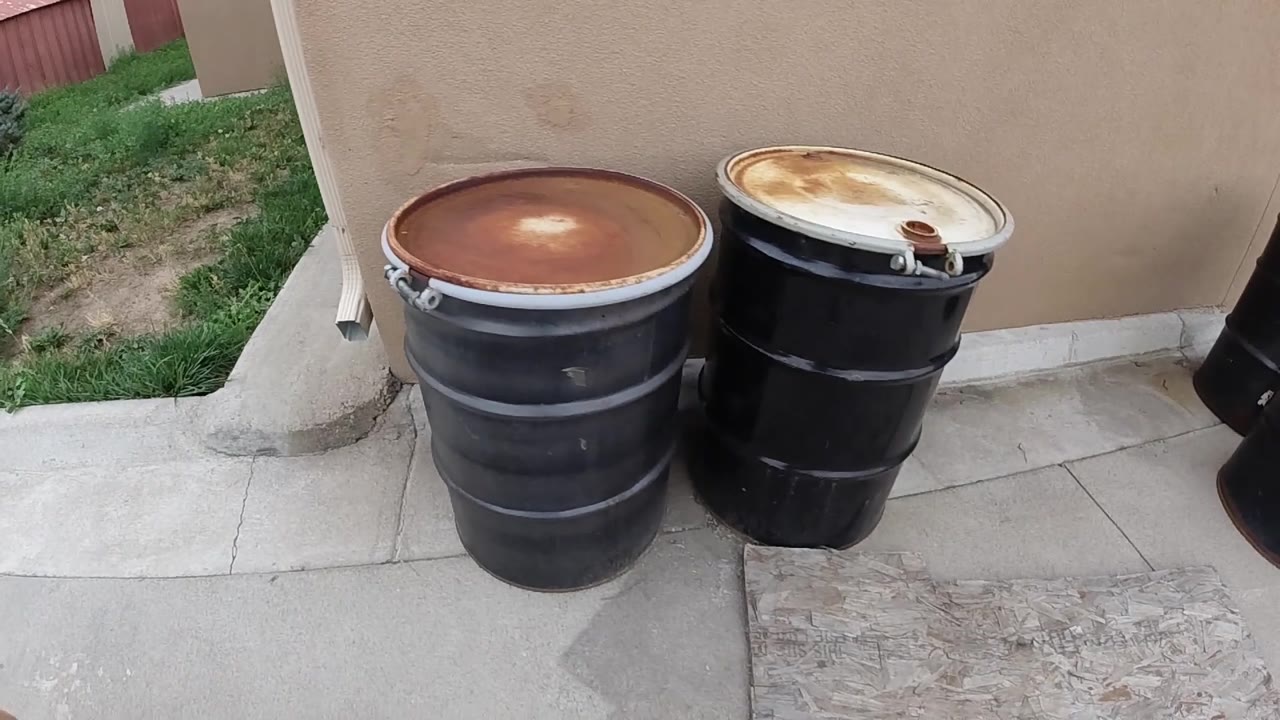 Two large black steel oil drums with corroded tops on a concrete pad against a tan stucco exterior building wall in Denver, Colorado; no visible people