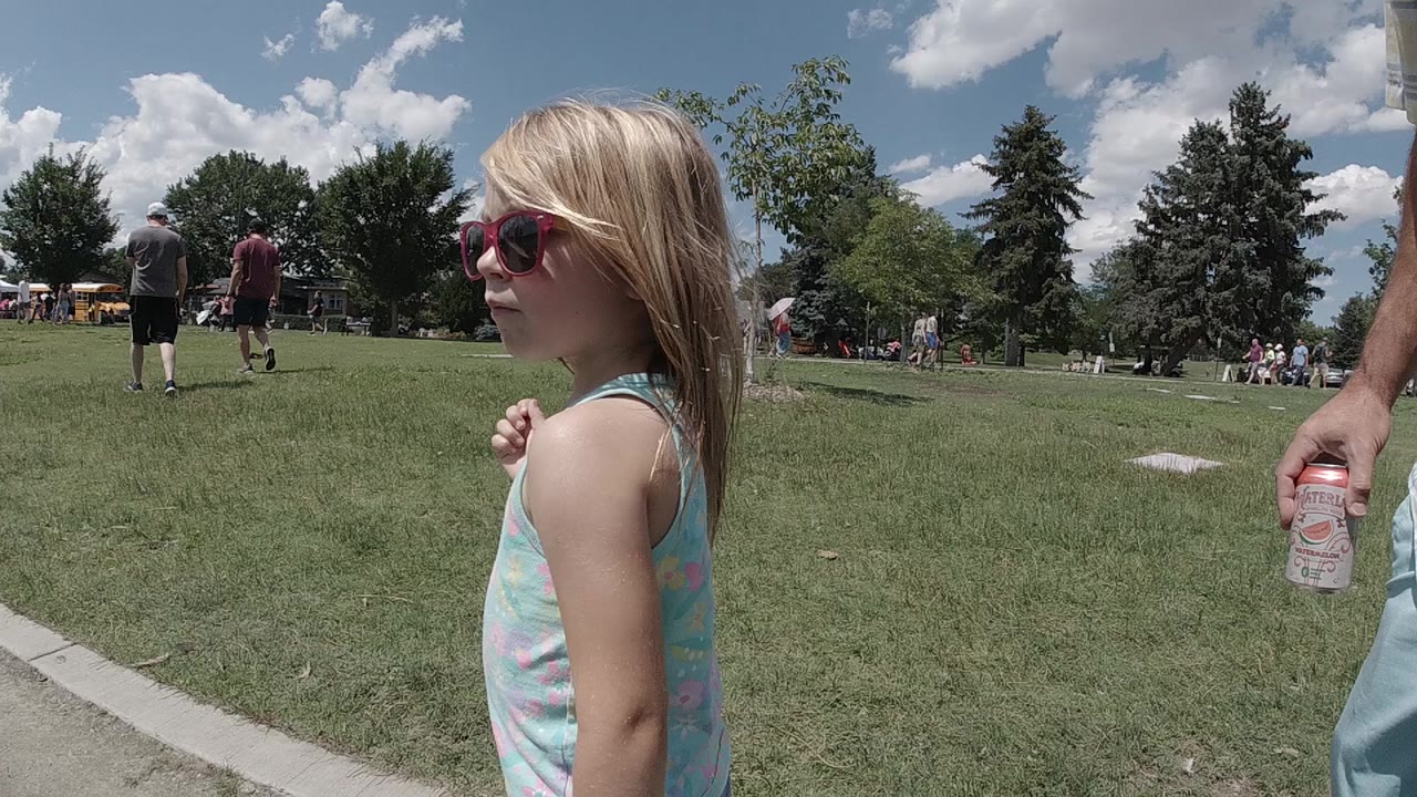 Blonde girl in red sunglasses walking beside a grassy park field.