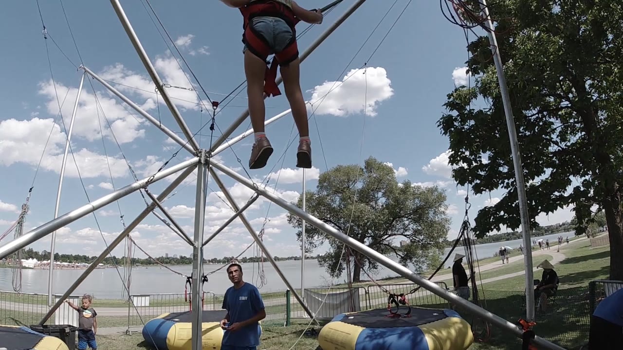 The girl reaches high near the top of the Denver carnival ride frame, while the attendant and a smaller child are visible below near the padded landing zones.