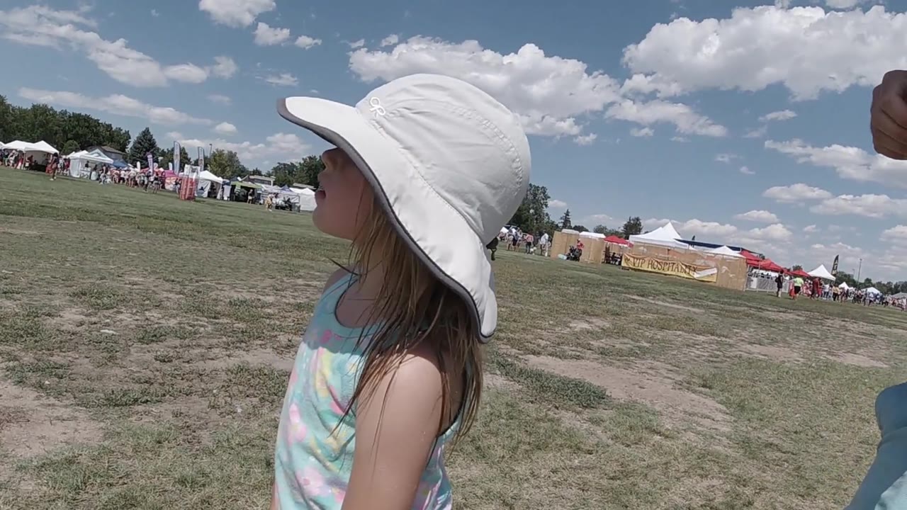 Young girl in profile under a white sun hat at a festival.