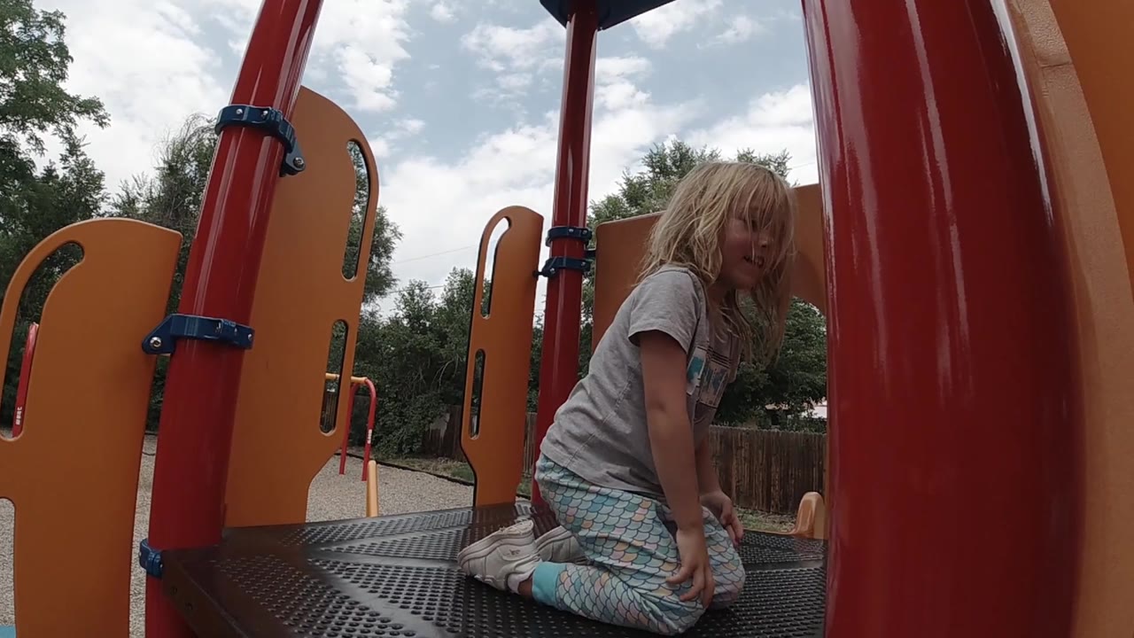Girl turns on a playground platform beside red supports.
