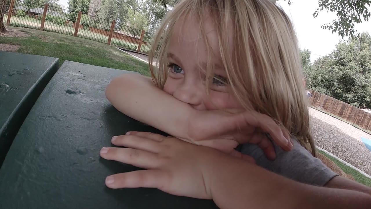 Child leaning on a picnic table with hair across her face.
