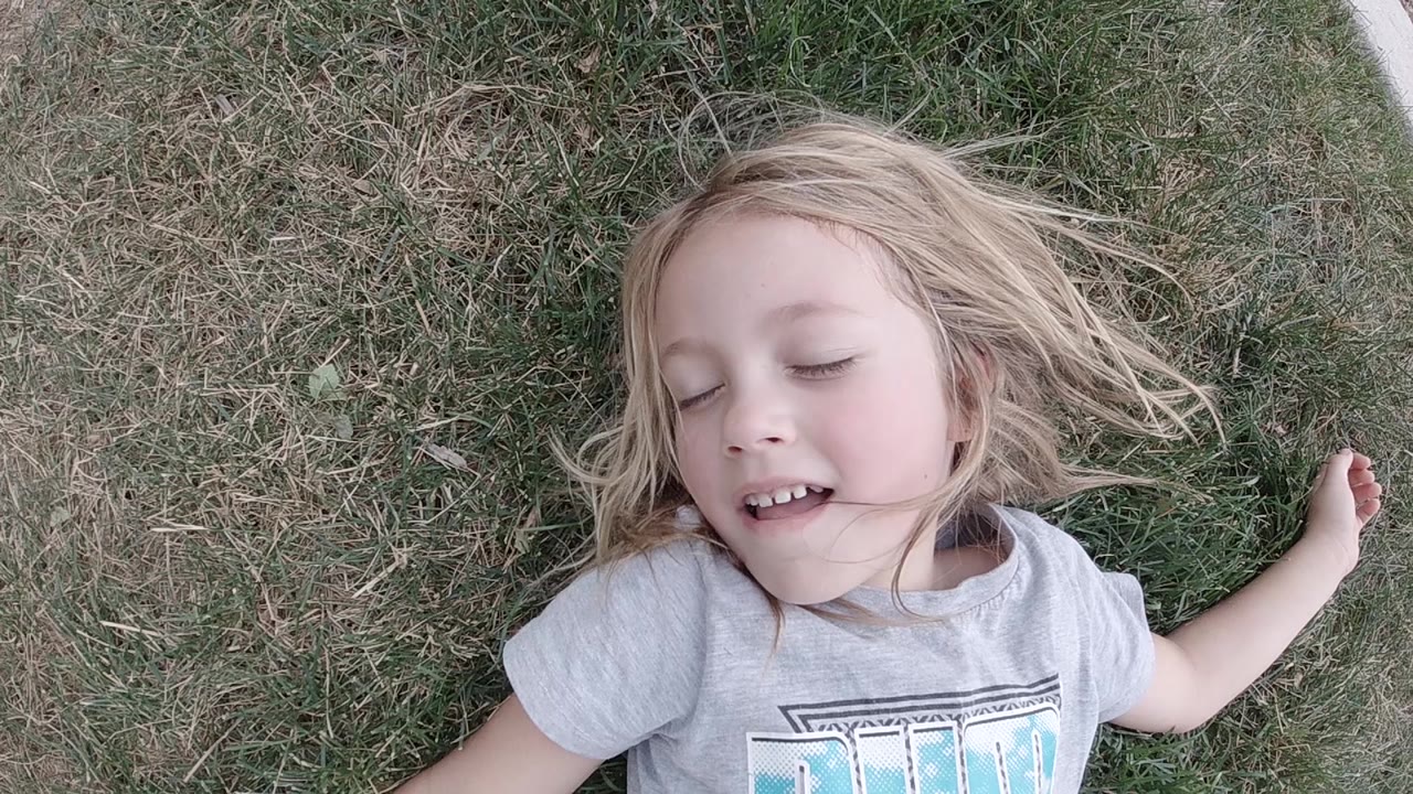The girl remains on the grass in San Jose Del Cabo with closed eyes, hair spread to one side and one bent arm near the edge of frame.