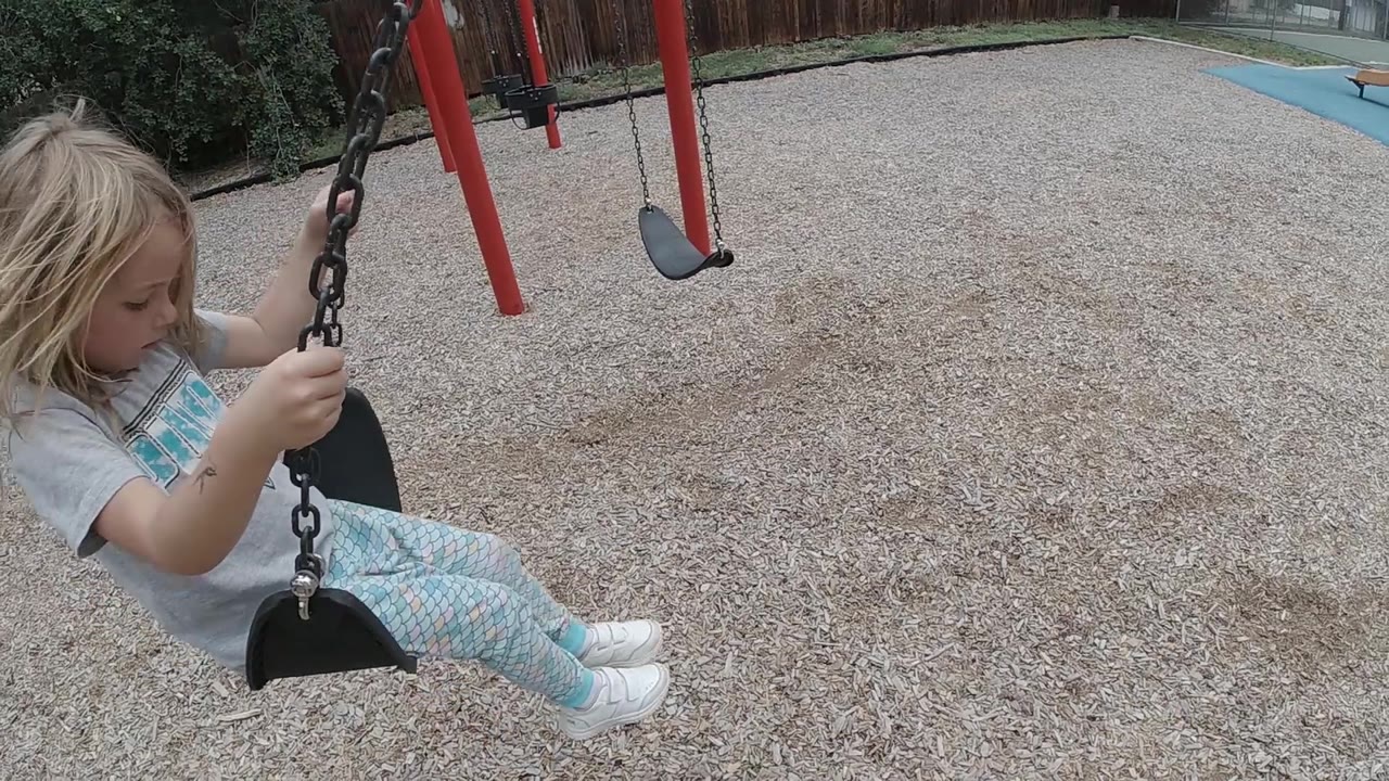 Child swinging forward over tan playground mulch