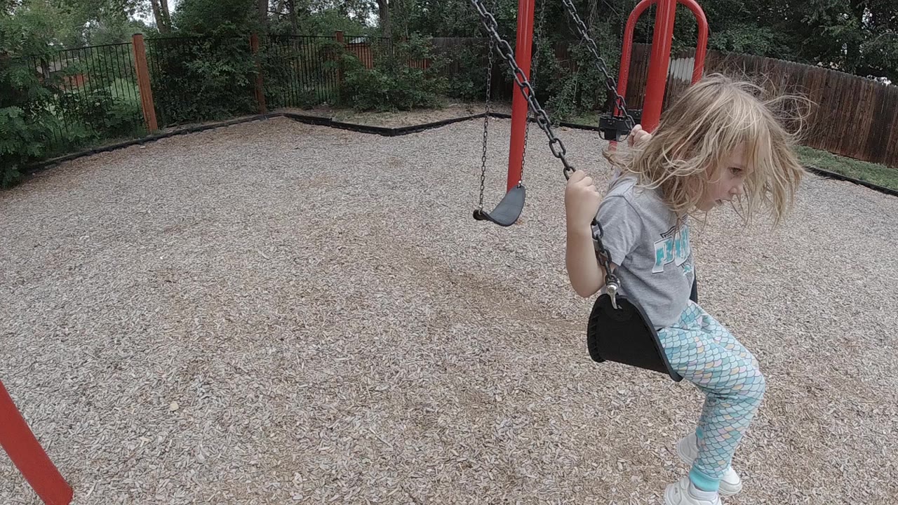 Blonde girl close to camera on a black playground swing.