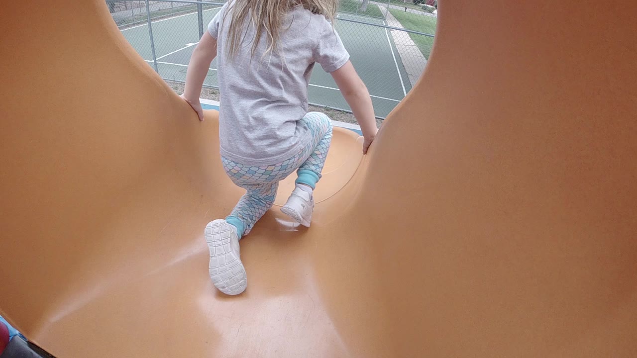 Child kneeling at the top of an orange playground slide.