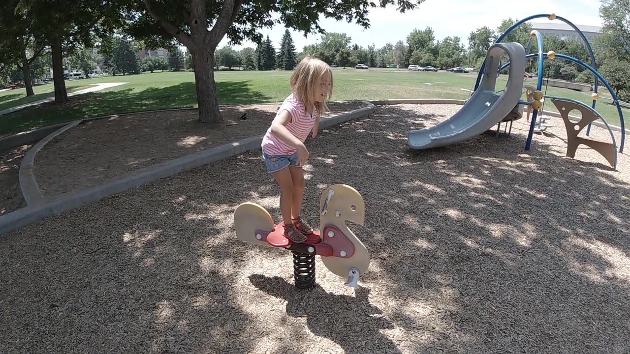 Child stands on rocker with slide behind her.