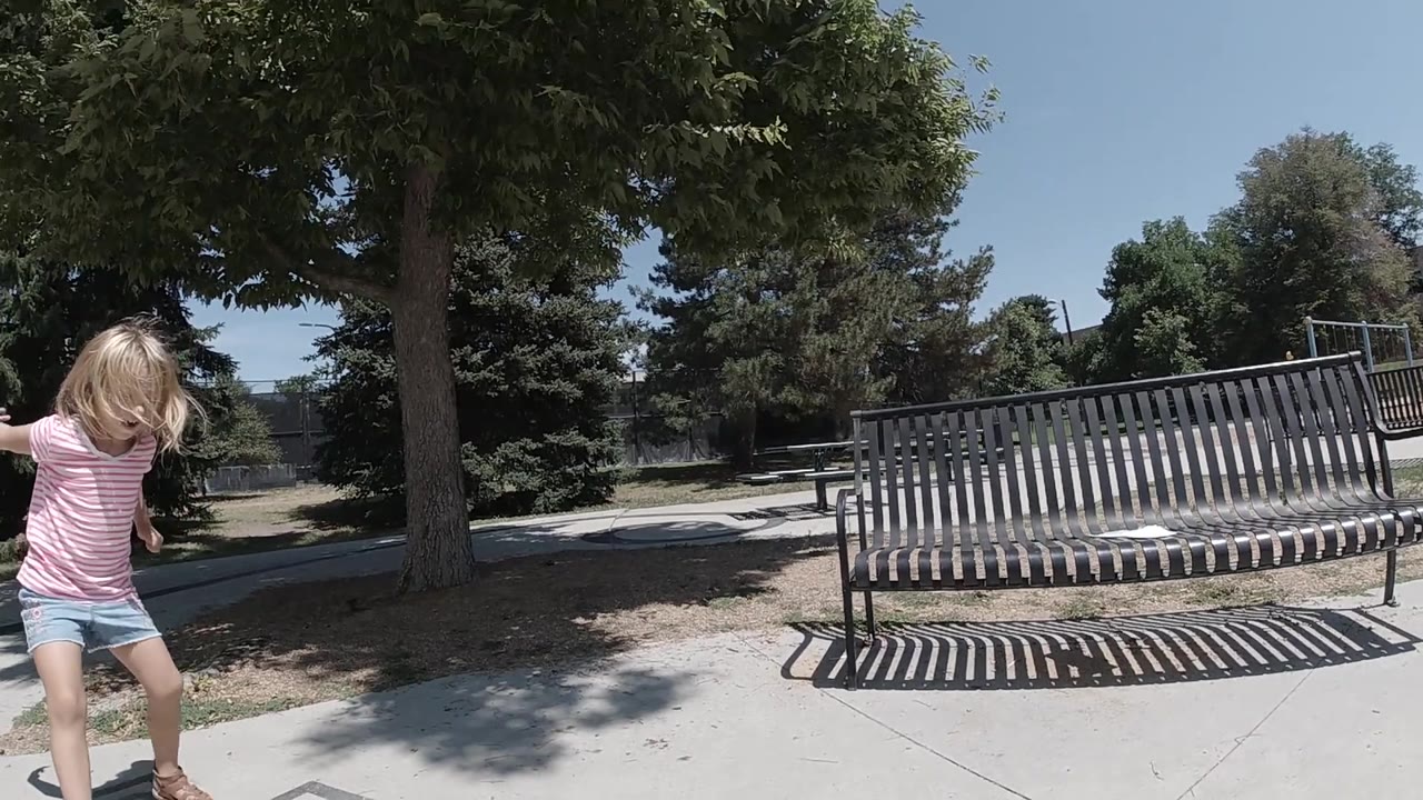 Child looks down while moving along the sidewalk near trees.