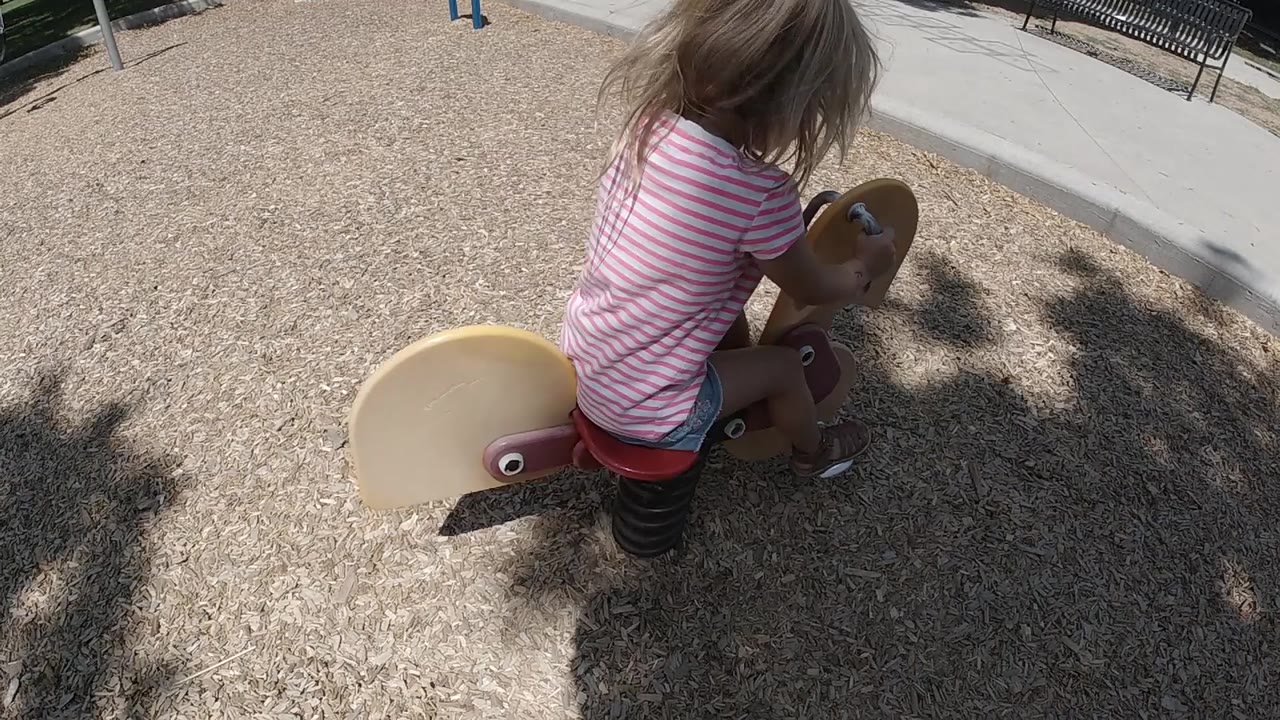 The child leans forward over the tan handle area of the wooden rider, with the red seat and dark spring base visible below.