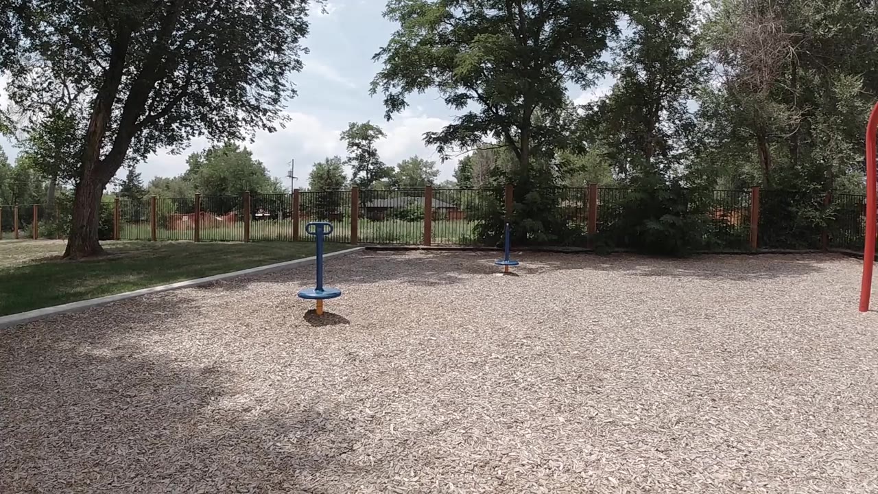 Wide gravel playground with blue spinner and trees.