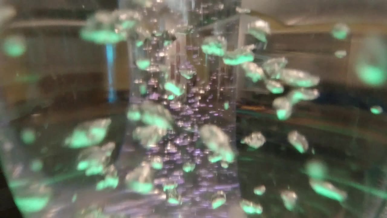 Bubbles gather around the central vertical column of the clear tube, with soft green highlights and no visible people.