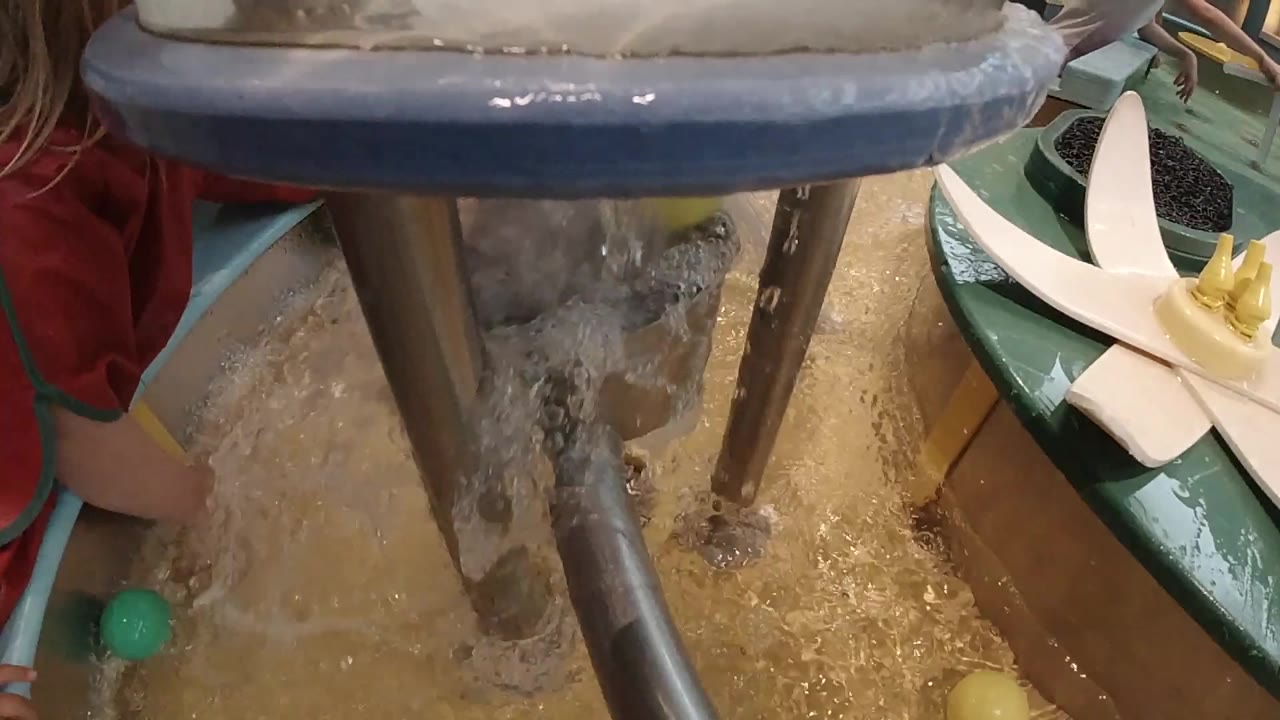 Water continues to churn below the blue rim and metal supports, while the child's red sleeve and arm remain partly visible on the left side.