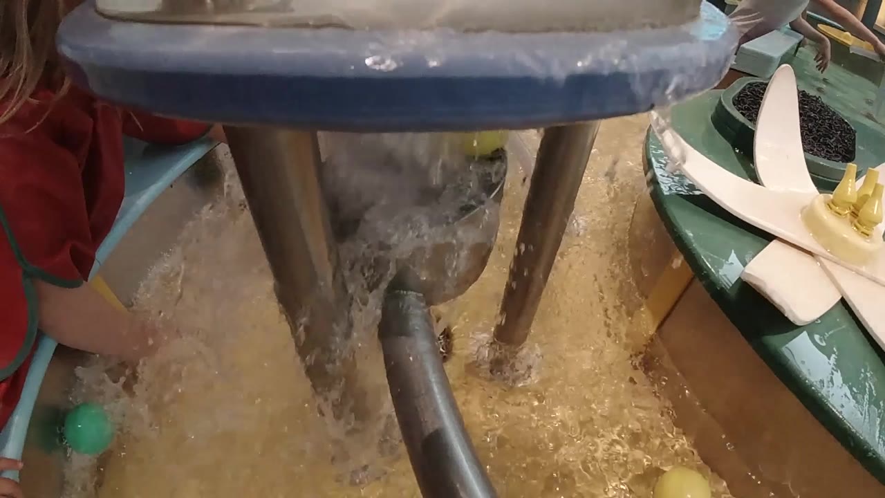 Foamy water falls between the tall metal posts, with the basin floor visible below and the child cropped along the left edge.