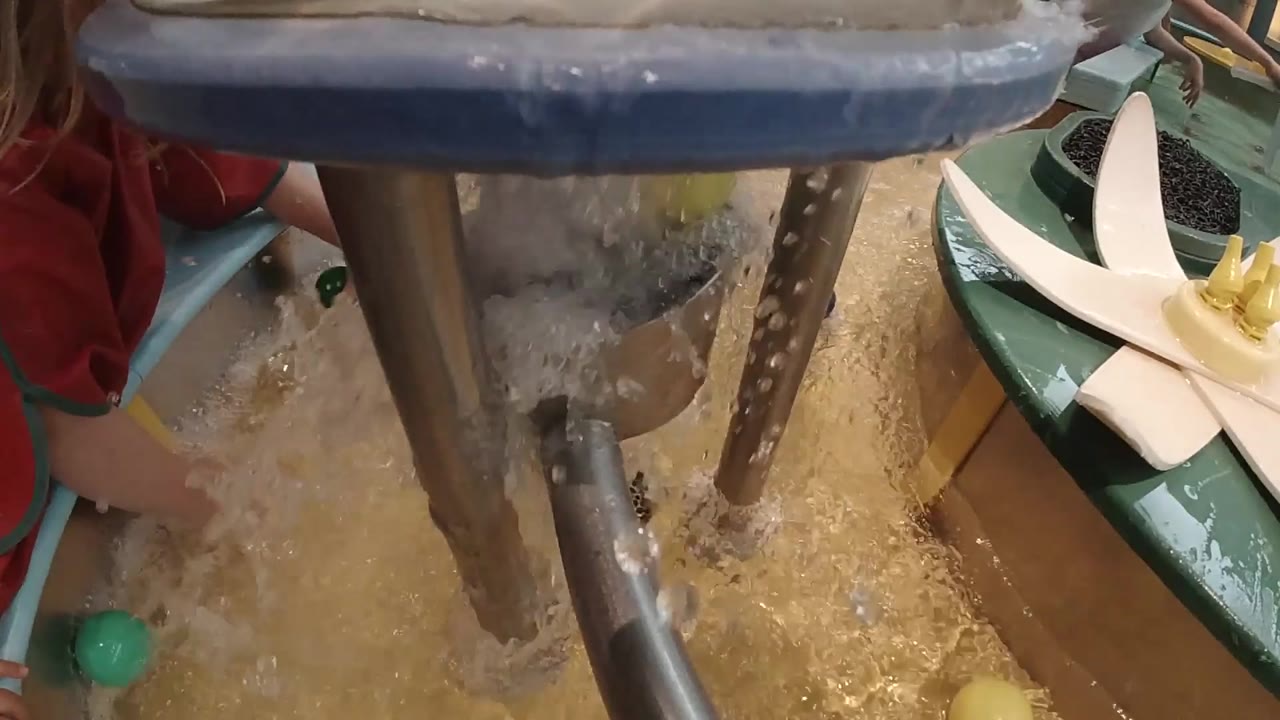Child's hand reaches near a green ball beside splashing water.