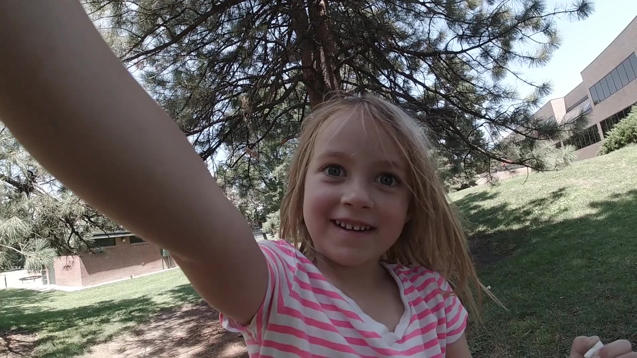Young blonde girl reaches toward the camera in a park.