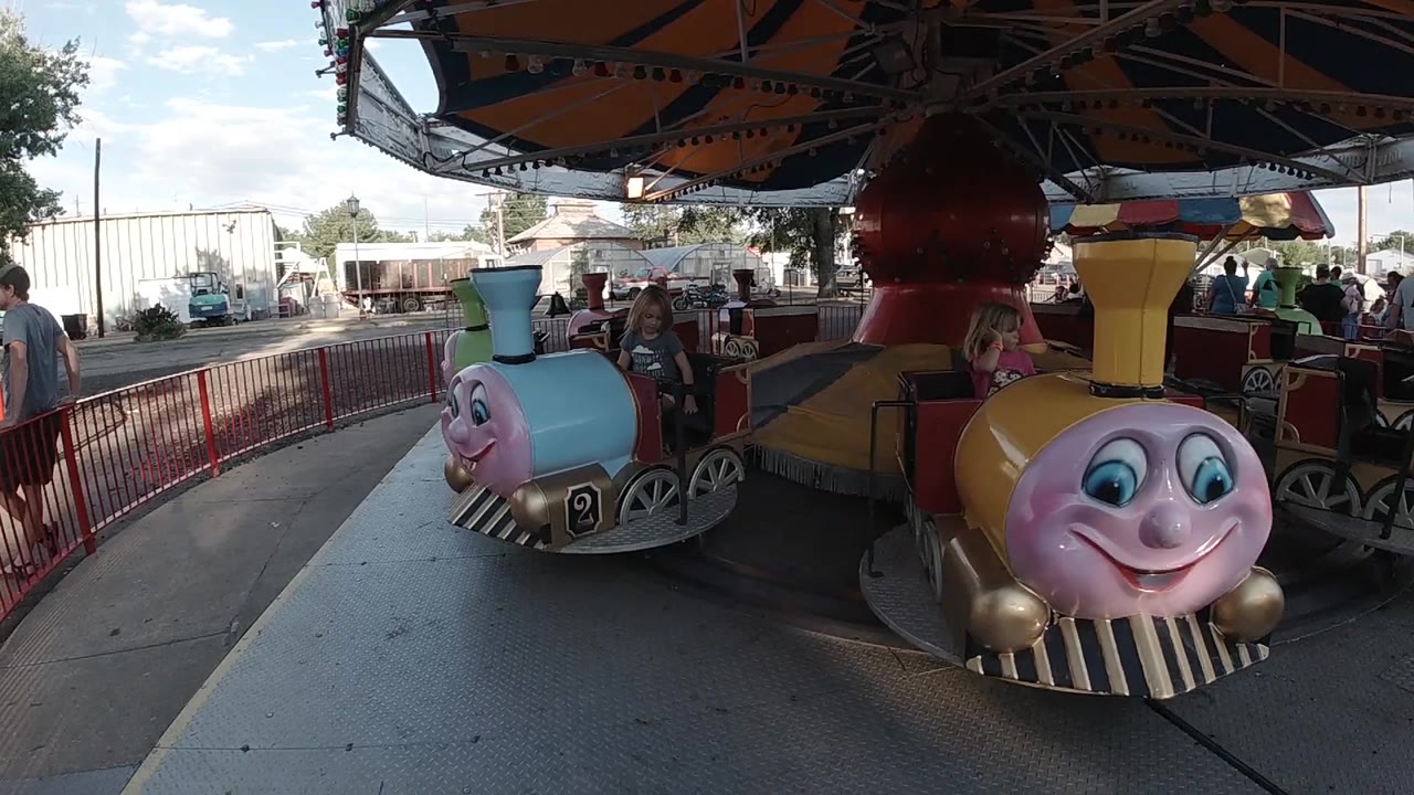 The yellow train car moves nearer the foreground as the blue car sits farther left on the circular ride at Lakeside Amusement Park in Denver.
