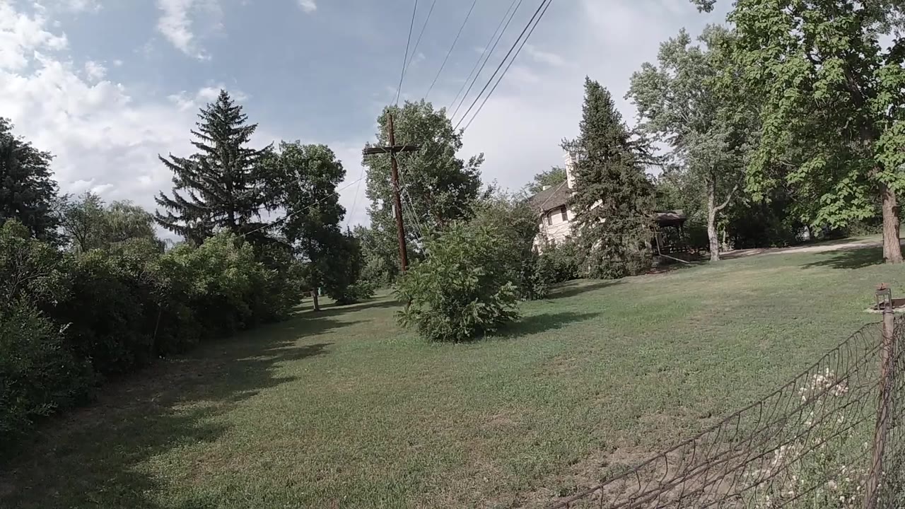 Green lawn with trees, wire fence, utility lines, and cloudy sky.