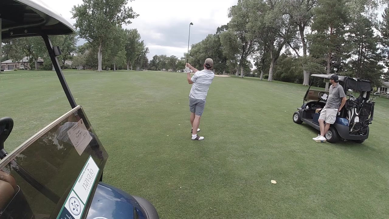 Golfer holding follow-through with a seated companion by the cart.