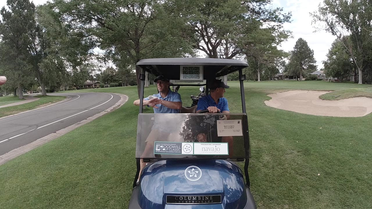 Two men riding in a blue golf cart on a golf course.