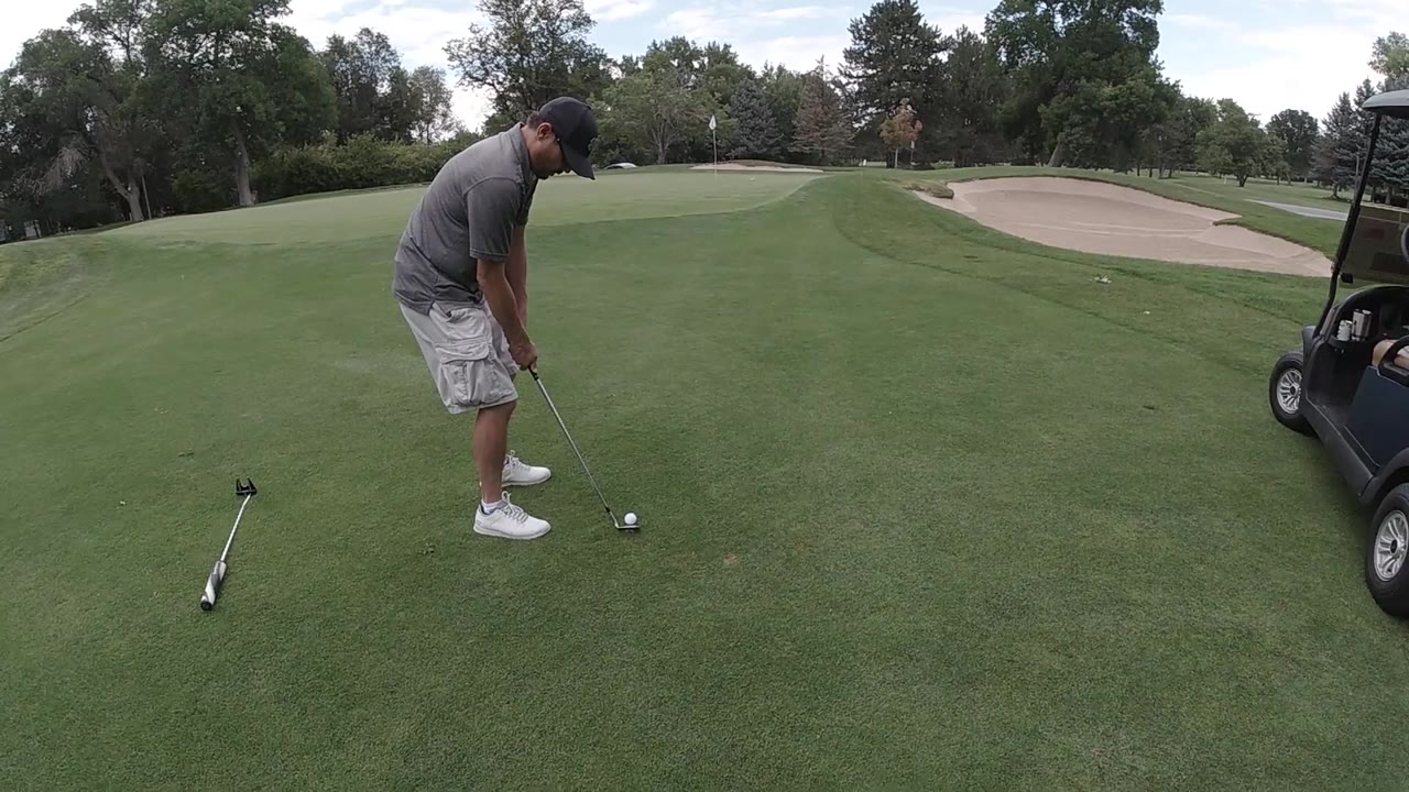 Golfer leans over the ball on a fairway near a sand trap.