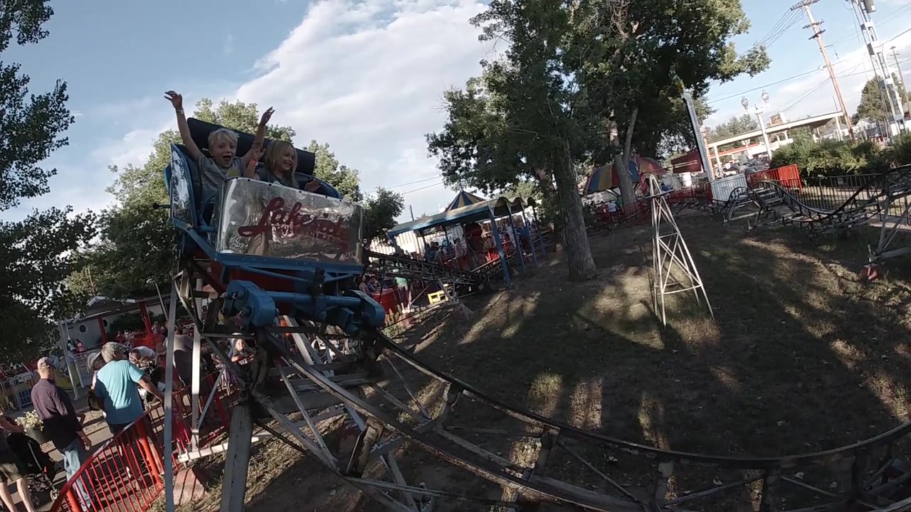 Front coaster car approaching with riders visible