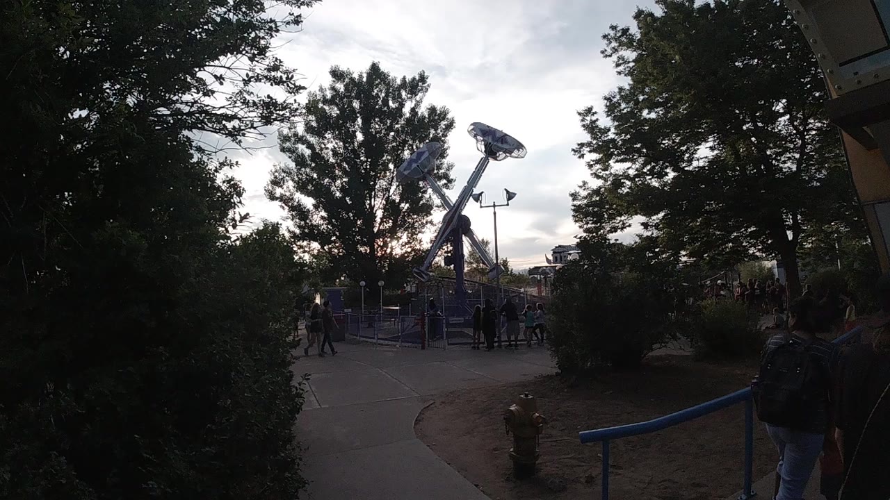 Tree-lined amusement park path with a blue ride ahead