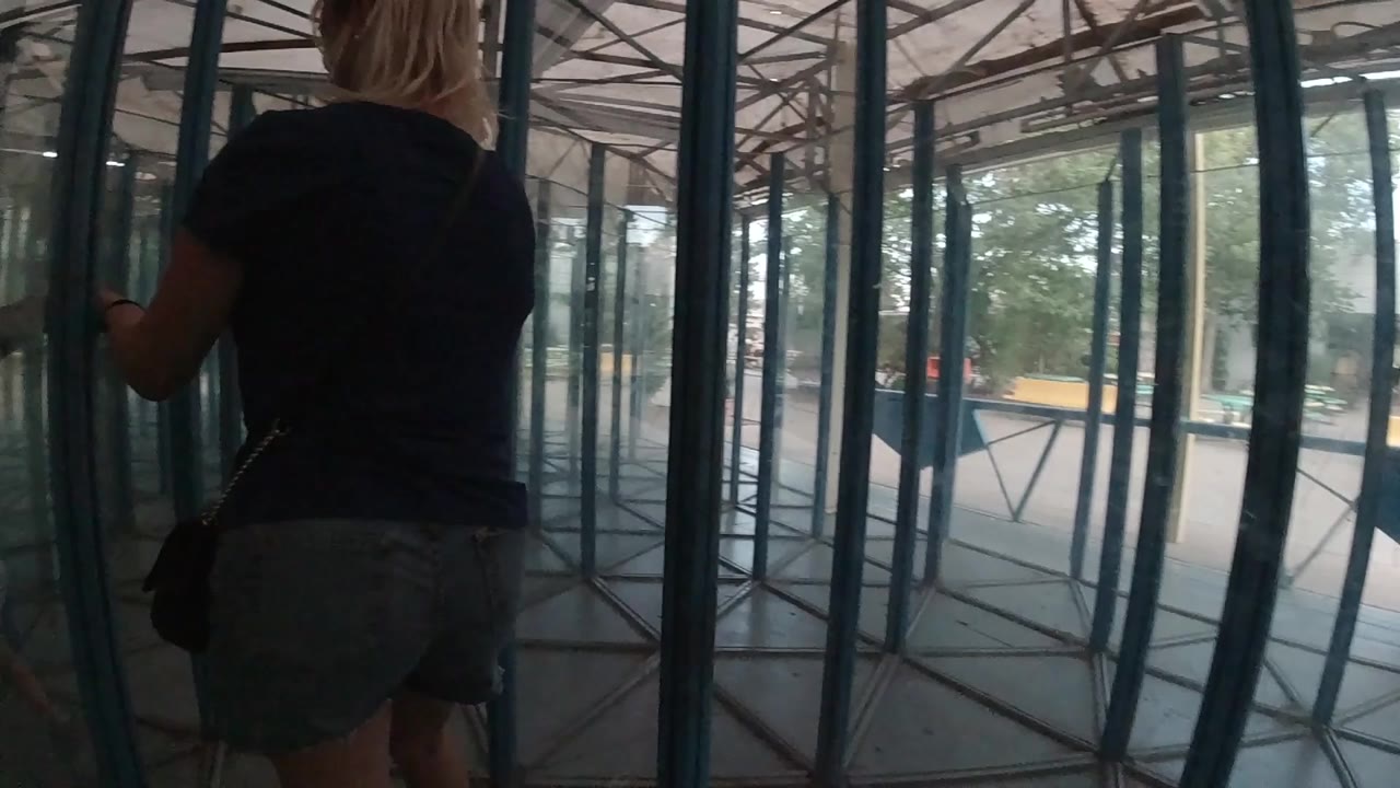 At the start of the Colorado clip, a blonde woman seen from behind enters a blue-framed glass corridor with daylight beyond the panels.
