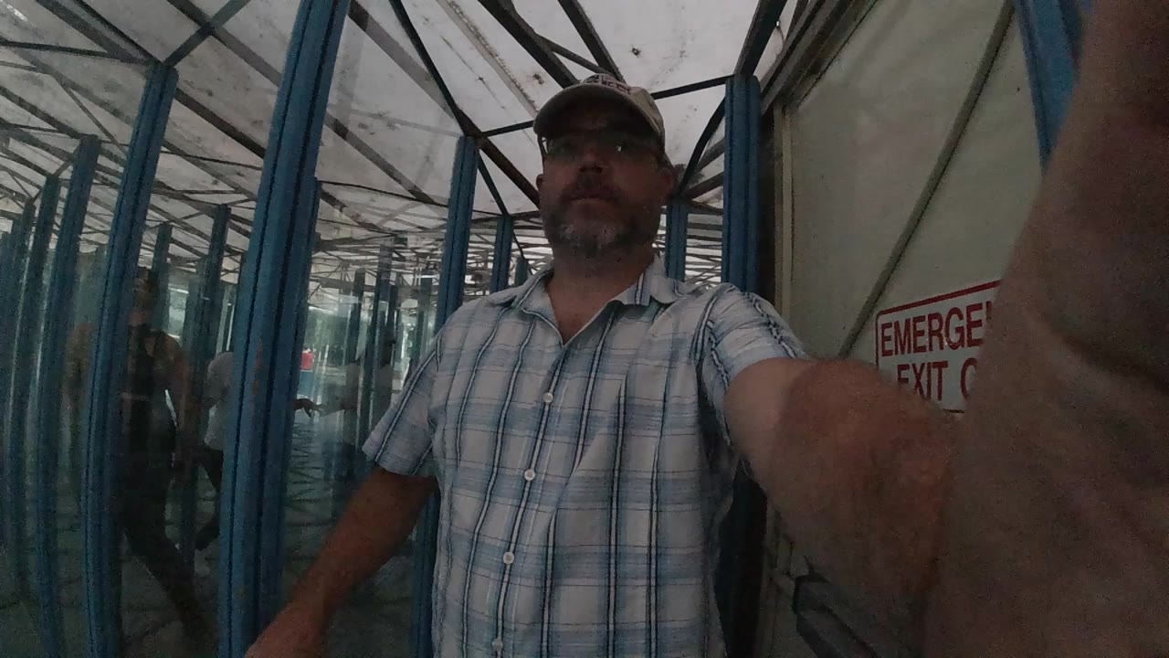 One second in, the man remains centered with his extended arm near the lens and repeated blue glass framing receding behind him.