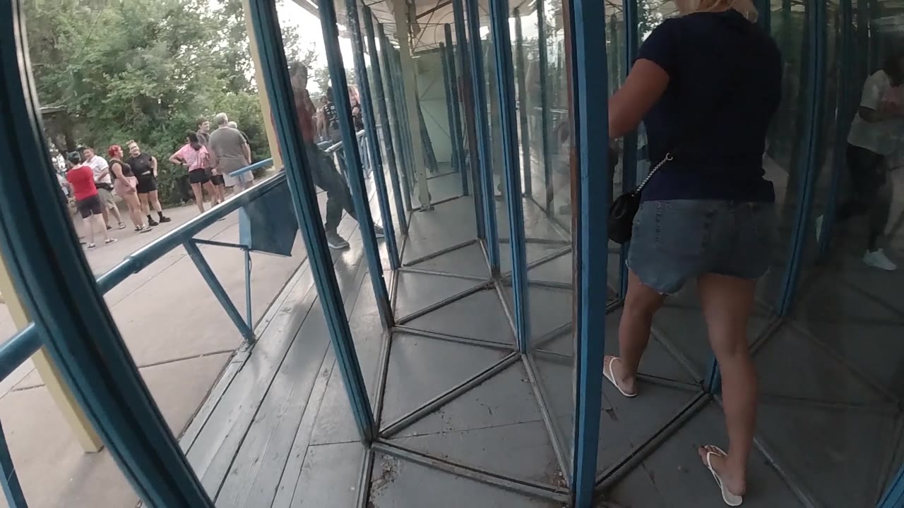 A woman stands close to the right side of the blue-framed glass exit while people and trees remain visible outside in the Colorado public setting.