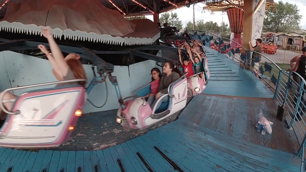 A pink car marked 7 moves across the foreground while more riders sit in following cars on the Denver amusement park ride.