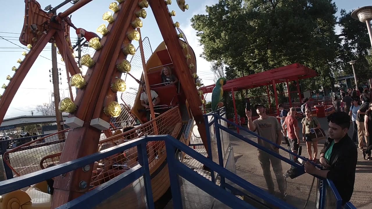Pirate ship ride beside blue railings with park visitors nearby.
