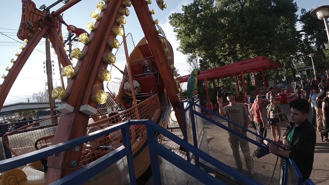 The pirate ship ride remains centered in Colorado, with yellow bulbs on the support arm, blue rails in front, and adults and children visible along the walkway.