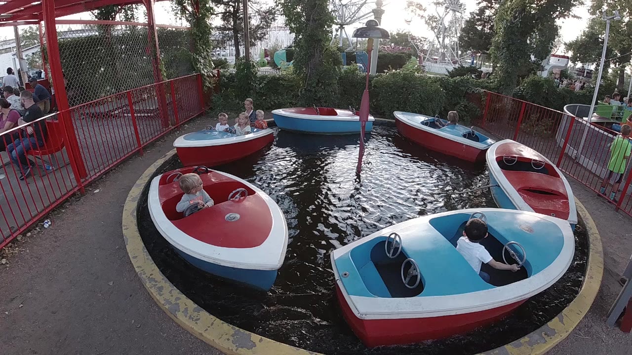 At the start of the Denver clip, red, white, and blue boats float in a small ride pool with children aboard and red railings around the basin.