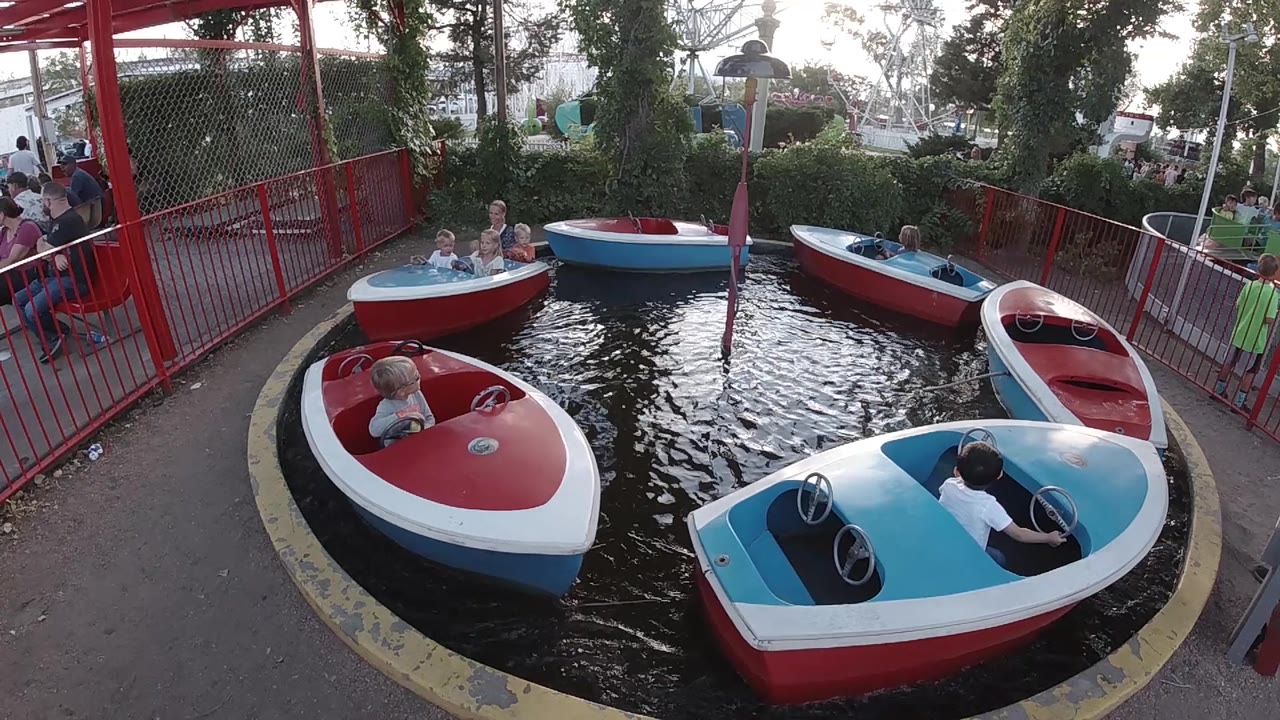 Children ride red and blue boats around a small pool.
