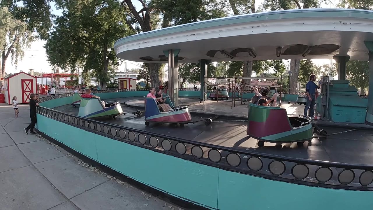 Boat carousel with a pink boat near the center and people on the ride.
