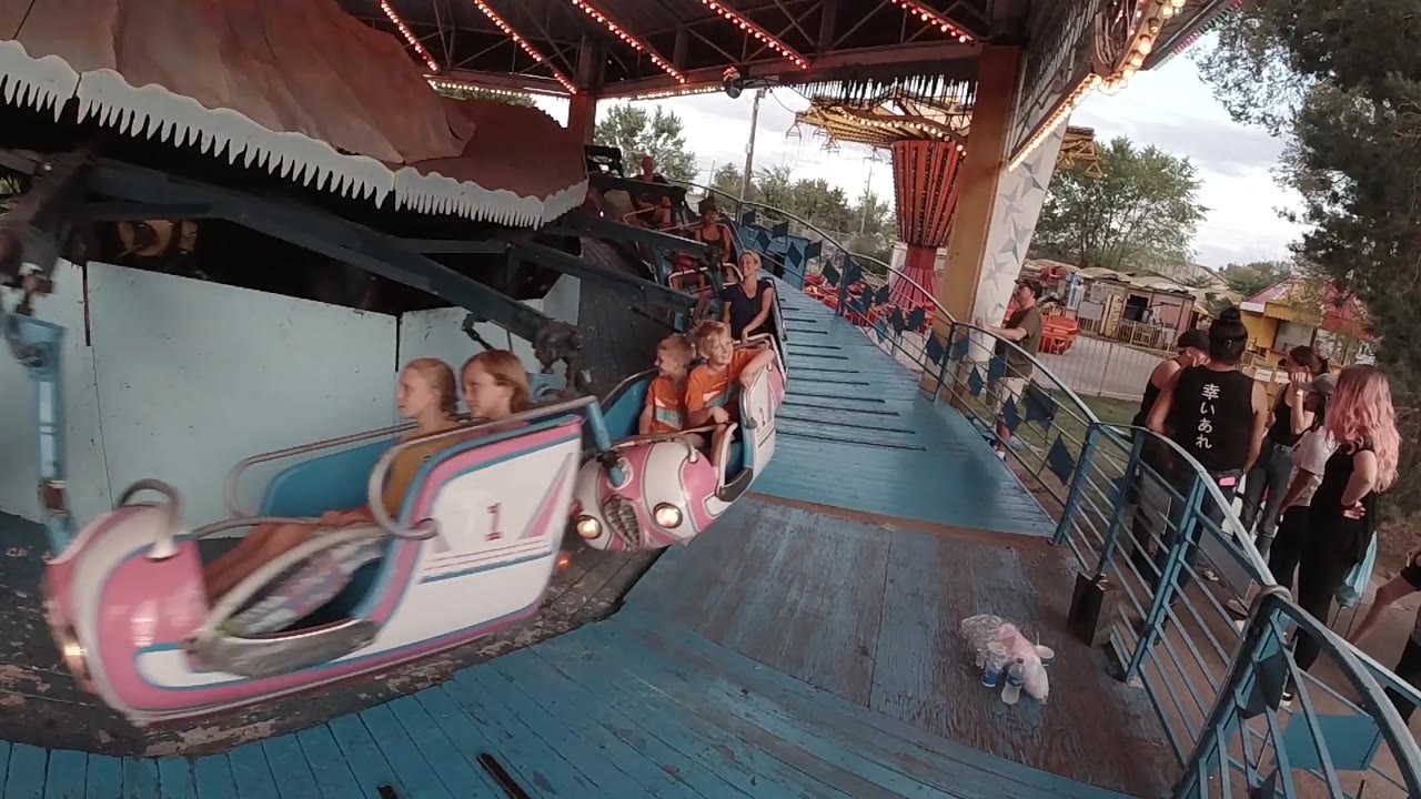 A white and pink ride car comes through the covered loading area in Colorado while adults and children are visible near the railing.