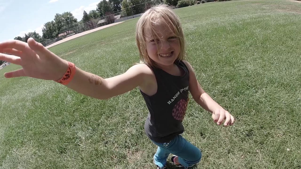 The girl remains close to the camera in Colorado, smiling as her hand reaches into the foreground over green grass.