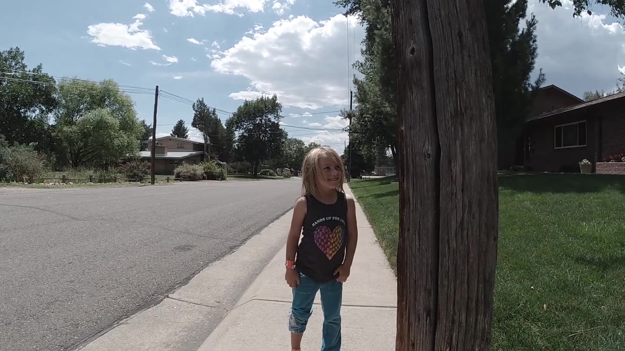 Girl on a sunny sidewalk with road and trees behind her.