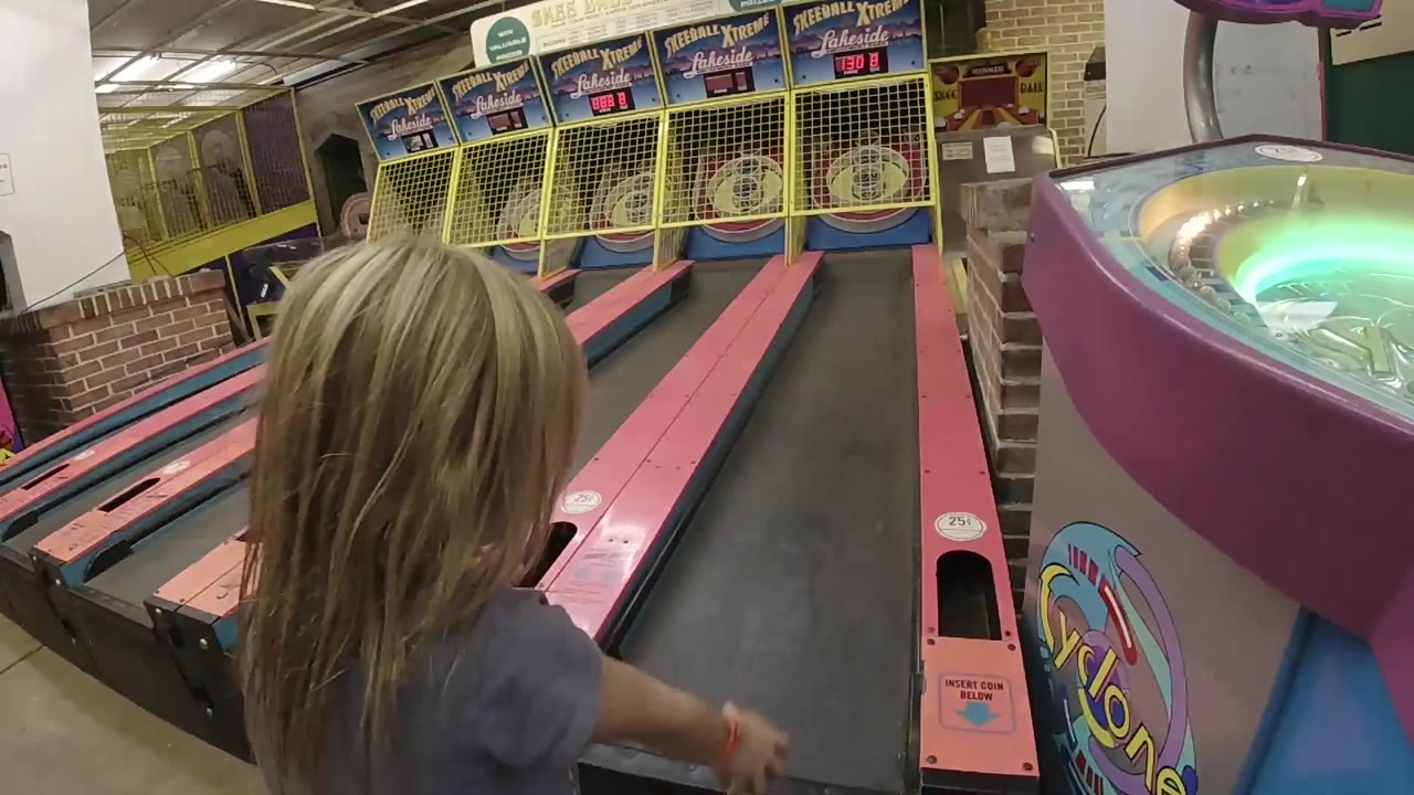 Girl leans over the skee-ball lane from the side.