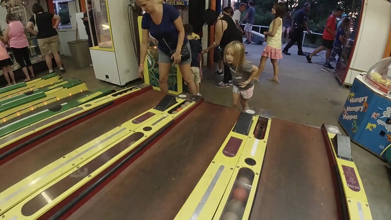 Skee-ball ball rolls in the foreground near a child