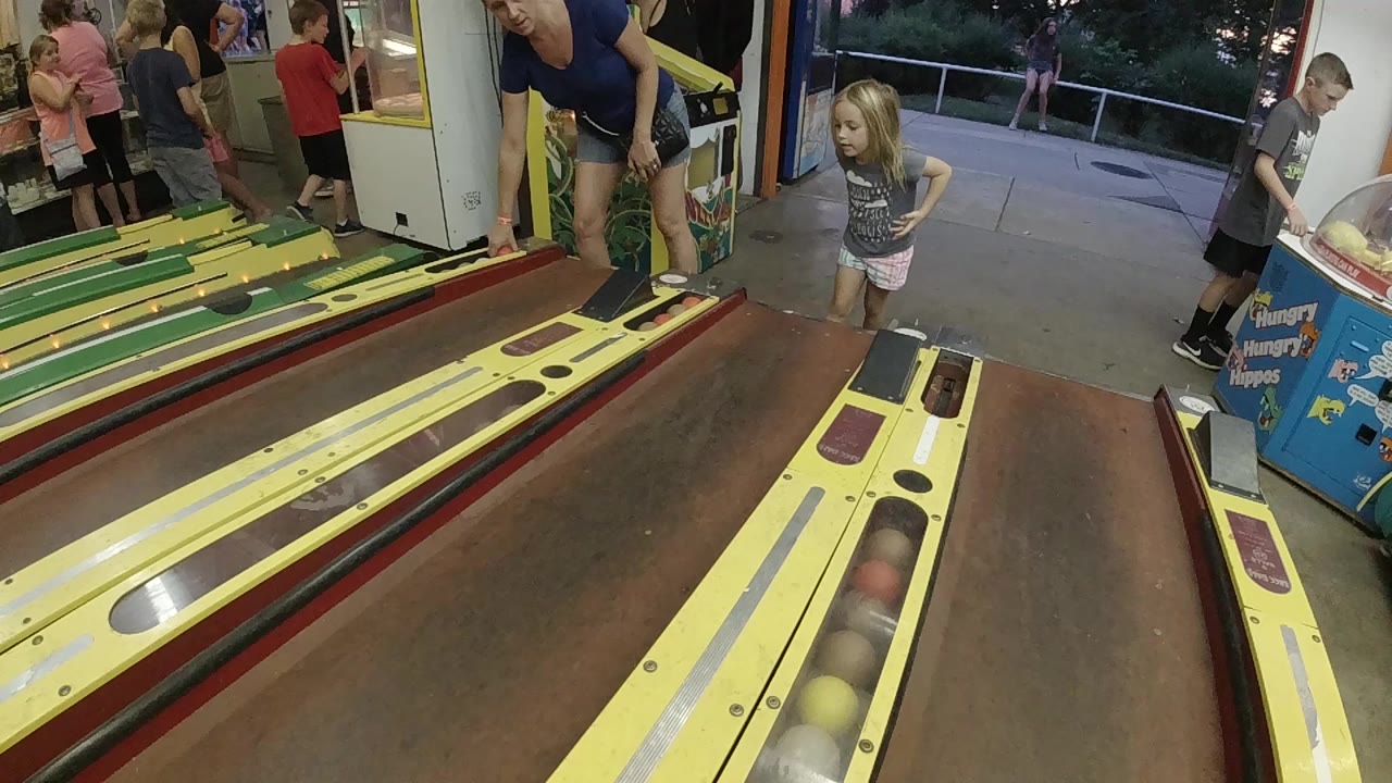 Child at yellow skee-ball lanes with adults nearby.