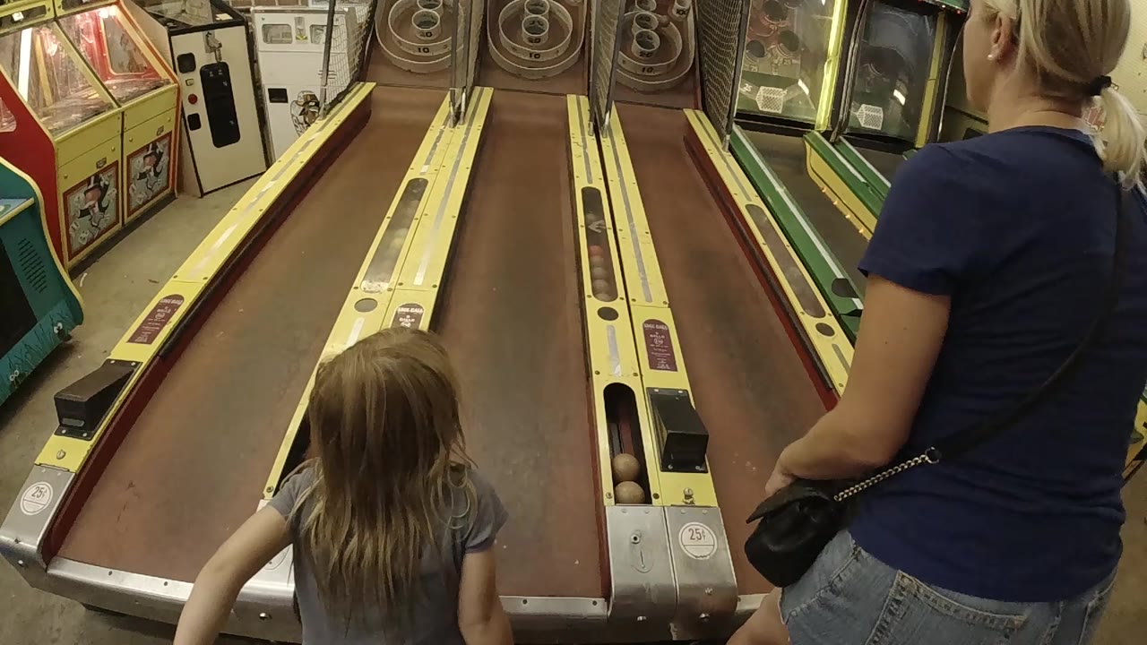 The young girl stands near the ball return while her mother watches from the right side of the Colorado arcade skee-ball lanes.