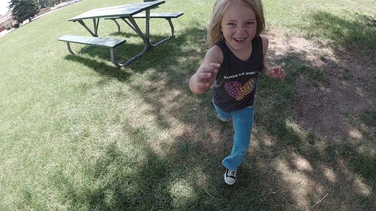 Young girl running toward the camera on grass near a picnic table.