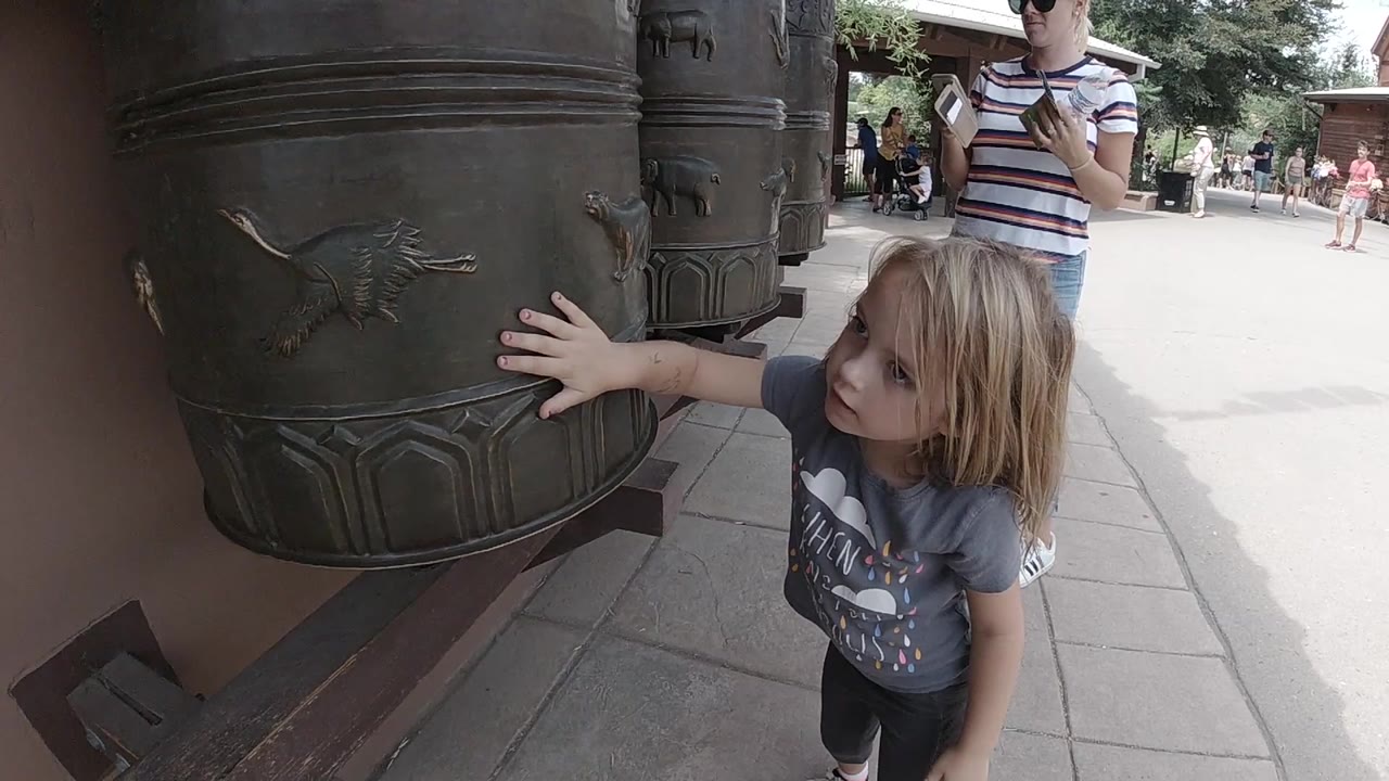 At the start in Denver, a young blonde girl places her hand on a dark metal cylindrical display with raised animal shapes while an adult stands behind her.