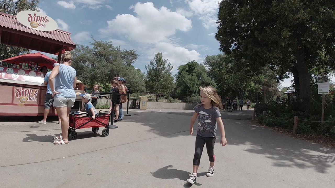 Girl continues walking in front of snack kiosk and trees