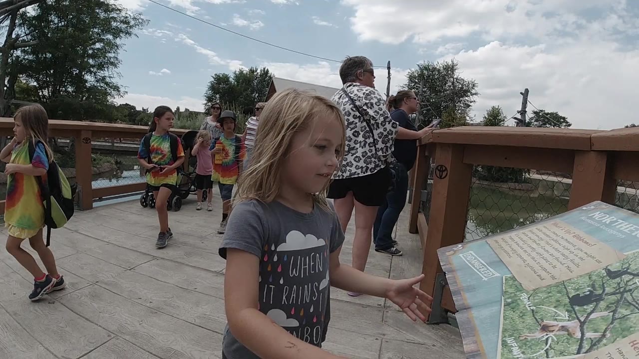 Young girl beside an outdoor information board with visitors behind her.